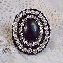 Bague Stone Noire avec un cabochon en Onyx orn&eacute; de chatons en Cristal &agrave; laquelle s&rsquo;ajoute des rocailles Argent&eacute;es qui compl&egrave;tent le Noir sur bague Nickel en Laiton et une feutrine. Un style R&eacute;tro